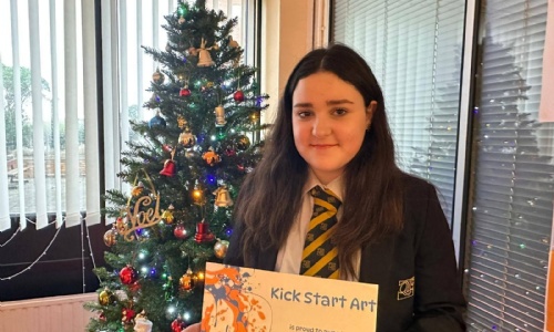 Picture of a Queen Elizabeth's winning student stood in front of a Christmas tree holding a certificate.