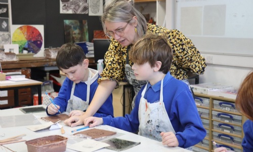 A Primary Pupil making a clay self-portrait at Sidmouth College with teacher helping 