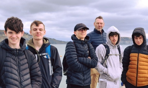 Tor Bridge High Students stood on the beach at Lyme Regis with a teacher. 
