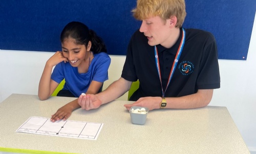 Member of staff from Whipton Barton Federation sat at a table teaching a pupil. 