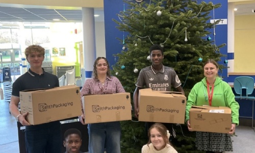 A group of students stood in front of a Christmas tree holding boxes of books