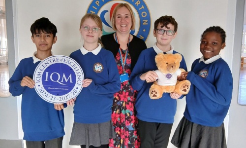 Students and a teacher have a picture taken with the IQM Award and a teddy. 