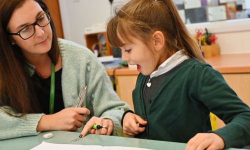 Student sitting at table being taught by a teacher