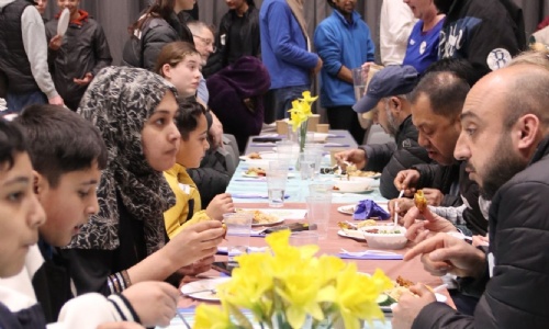 Exmouth Community sat at tables sharing food and talking with daffodils on the table 