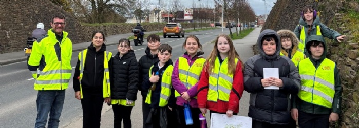 Group of students standing in hi-vis underneath the 'Welcome to Sherford' sign. 