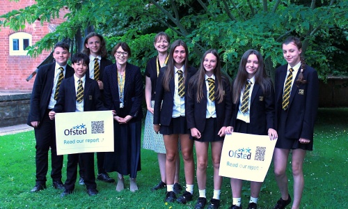 Group of students and staff holding Ofsted posters and smiling.