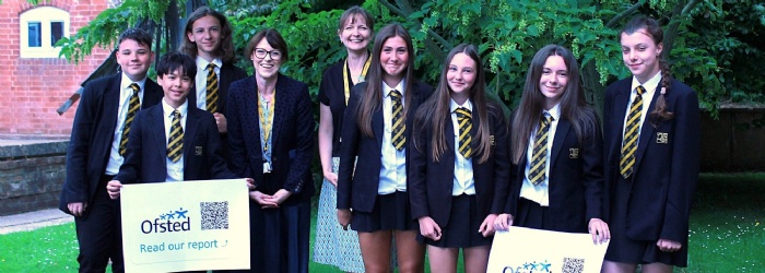 Group of students and staff holding Ofsted posters and smiling.